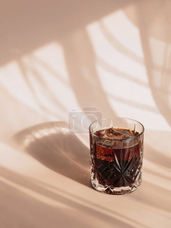 Photo for Whiskey cola cocktail with strong alcohol and ice in highball glass on light beige background with shadows and fantastic highlights and reflecting sunlight in daytime - Royalty Free Image