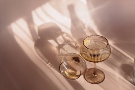 Two glasses with white wine placed on light beige background with shadows and fantastic highlights and reflecting bright sunlight in daytime