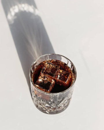 Whiskey cola cocktail with strong alcohol and ice in highball glass on white background with hard light
