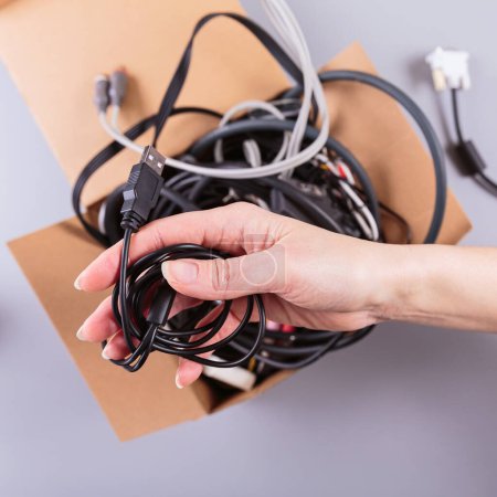 Female hands carefully packing discarded cables and wires into a cardboard box, promoting eco-friendly recycling practices