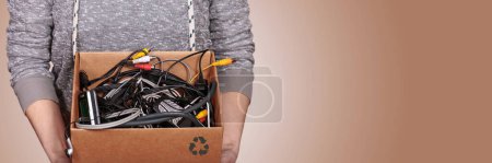 Womans hands holding a recycling box filled with old cables and wires, exemplifying a commitment to environmental conservation