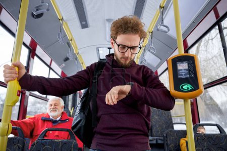 Foto de Portrait of ginger curly haired wearing glasses and wrist watch in aubergine sweater male rushing trying to fasten with urban transport. Hasty rythm of life people make too many plans getting nervous - Imagen libre de derechos