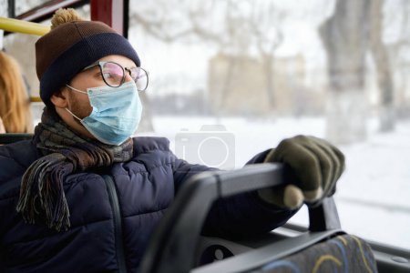 Photo for Side view of passenger traveling by bus during global pandemic, wearing medical mask, protecting. Young man wearing glasses, sitting, holding. Conept of quarantine measures. - Royalty Free Image