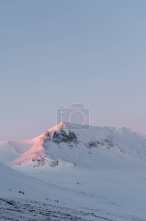 Light pink sunrise alpenglow on a snowy mountainside in Sweden