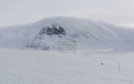 Markierungen der Langlaufloipen, halb im Schnee vergraben, zeigen den Schwur durch das Sylarna-Gebirge. Im Hintergrund ziehen Gewitterwolken über den Berg.