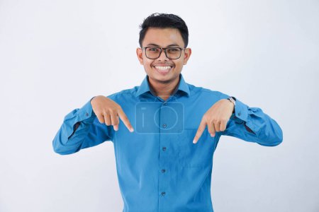Foto de Hermoso asiático empleado masculino con gafas sonriendo en dedo apuntando hacia abajo pose usando camisa azul aislado sobre fondo blanco - Imagen libre de derechos