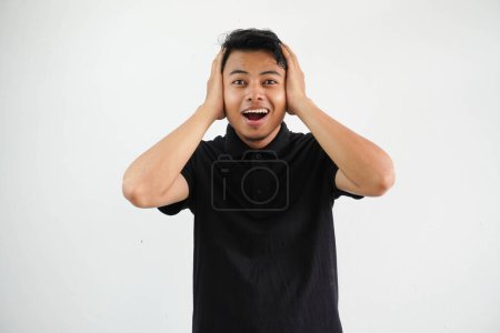 young asian man both hands holding the head screaming, very excited, passionate, satisfied with something, wearing black polo t shirt isolated on white background