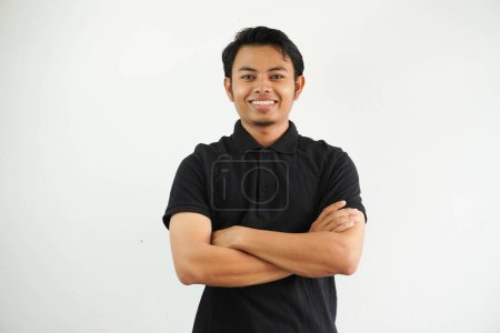 Foto de Joven asiático hombre sonriendo feliz en la cámara con brazos cruzados usando negro polo camiseta aislado en blanco fondo - Imagen libre de derechos