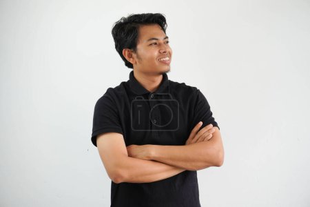 Téléchargez les photos : Jeune asiatique homme souriant heureux à la caméra avec les bras croisés portant noir polo t-shirt isolé sur fond blanc - en image libre de droit