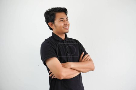 Foto de Joven asiático hombre sonriendo feliz en la cámara con brazos cruzados usando negro polo camiseta aislado en blanco fondo - Imagen libre de derechos