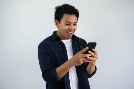 Photo for Smiling young asian man looking to his mobile phone with happy expression isolated on white background - Royalty Free Image