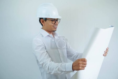Téléchargez les photos : Jeune asiatique mâle architecte ingénieur sourire et tenant ingénierie plans isolés sur fond blanc. - en image libre de droit