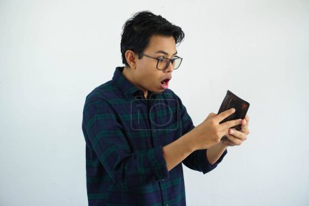 Foto de Joven asiático hombre mostrando impactado cara expresión mientras mirando a su billetera aislado en blanco fondo - Imagen libre de derechos