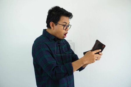 Téléchargez les photos : Jeune asiatique homme montrant choqué visage expression tout en regardant à son portefeuille isolé sur fond blanc - en image libre de droit