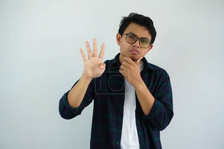 Photo for Young asian man showing curious face expression while giving four fingers sign isolated on white background - Royalty Free Image