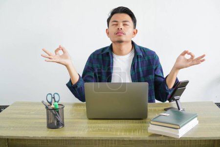 un asiático macho freelancer es sentado mostrando un gesto zen posición