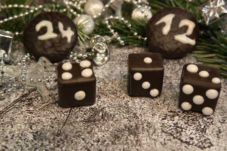 Dominoes with dots that look like dice in front of fir greenery, Christmas decorations and chocolate cookies with the date of Christmas Eve