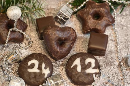 Dominoes and chocolate cookies with the date of Christmas Eve in front of the Christmas decorations