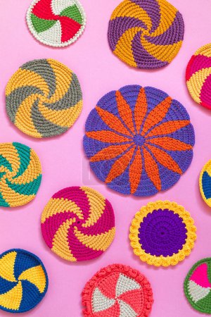 Bright colorful round crochet holders and cup coasters on a pink background. Home craft. Handmade kitchen decor. Top view.