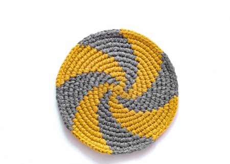 Grey yellow round spiral cup coaster on a white background. Crochet stand for hot. Kitchen tools and accessories. Modern handmade concept. Copy space. Top view.