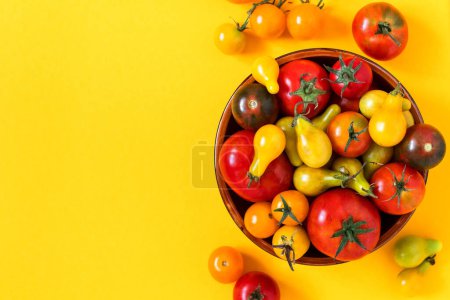 Bowl with tomatoes of various varieties and colors on a yellow background. Organic red tomatoes, yellow pear tomatoes, cherry tomatoes. Top view. Copy space.