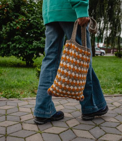 Téléchargez les photos : A woman walks with a crocheted bag. Tricolor pattern entrelak bound by Tunisian knitting. - en image libre de droit