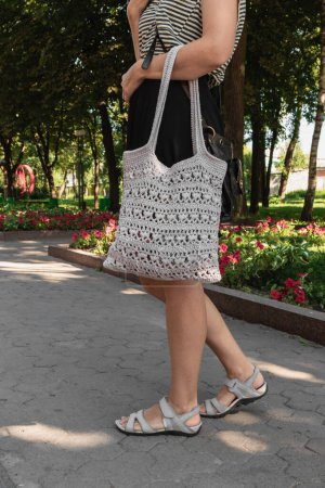 Téléchargez les photos : Light openwork women's handmade bag on a woman's hand during a city walk. Bag crocheted. - en image libre de droit