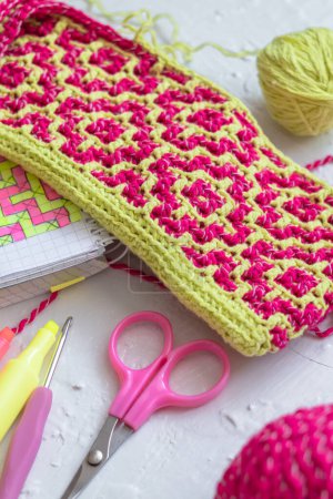Foto de Geometric ethnic pattern. Rhombus - bright pink yellow canvas. Workingplace with crochet fabric, crochet hook, notebook, scissors. - Imagen libre de derechos