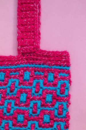 Foto de Eco friendly knit bag for shopping. Pink blue crochet bag with mosaic geometric pattern on a pink background. Zero waste concept. - Imagen libre de derechos