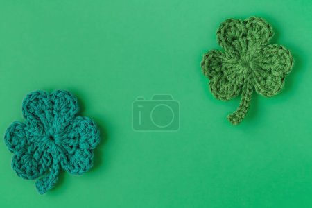 Photo for Happy St. Patrick's day decoration. Two green crochet shamrocks or clover leaves on a green background. Top view. Copy space. - Royalty Free Image
