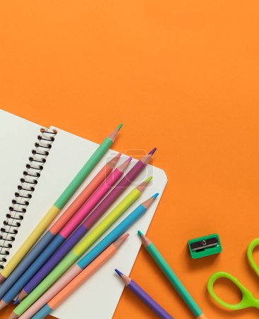 Téléchargez les photos : Crayon lumineux pastel double extrémité avec ciseaux, cahier et taille-crayon sur fond orange. - en image libre de droit