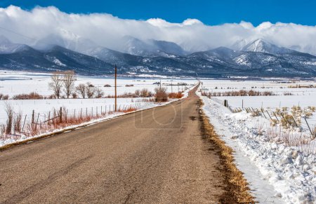 Photo for A rural country road through snow covered ranchland leads to the even more snow covered mountains of the Sangre de Cristo range in the Colorado Rocky Mountains. - Royalty Free Image
