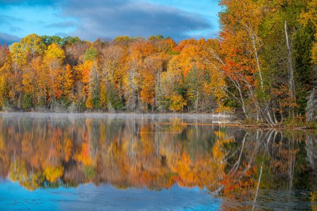 Téléchargez les photos : Belles couleurs d'automne reflétées dans l'eau d'un lac du nord du Wisconsin avec une brume matinale planant au-dessus de l'eau. - en image libre de droit