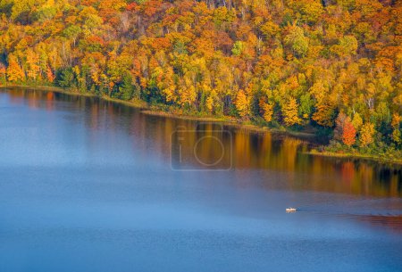 Photo for A lone boater sets out across the Lake of the Clouds in the Upper Peninsula of Michigan, the autumn colors surrounding the lake. - Royalty Free Image
