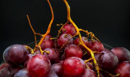 Téléchargez les photos : Photo de raisins dans un bol sur fond de couleur noire - en image libre de droit