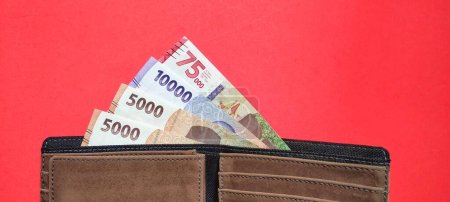 Téléchargez les photos : Vue de dessus d'un portefeuille contenant de nouveaux billets indonésiens émis en 2022. Rupiah concept de monnaie isolé sur fond rouge - en image libre de droit