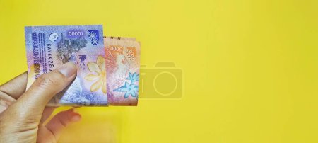 Téléchargez les photos : Homme tenant de nouveaux billets indonésiens, concept de monnaie rupiah isolé sur fond jaune. - en image libre de droit