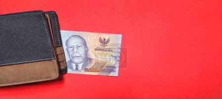 Téléchargez les photos : Un portefeuille et de nouveaux billets émis en 2022 Rp.10,000. Monnaie rupiah isolé sur un fond rouge. Vue du dessus - en image libre de droit