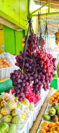Téléchargez les photos : Portrait de plusieurs grappes de raisins suspendues dans la boutique de fruits, il y a aussi d'autres fruits que l'on peut voir derrière - en image libre de droit