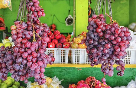 Téléchargez les photos : Plusieurs grappes de raisins suspendues dans la boutique de fruits, il y a aussi d'autres fruits qui peuvent être vus derrière - en image libre de droit