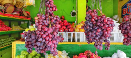 Photo for Several bunches of grapes hanging in the fruit shop, there are also other fruits that can be seen behind - Royalty Free Image
