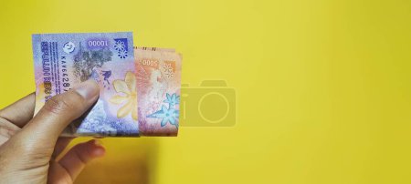 Foto de Hombre posee nuevos billetes de rupias rp5000 y rp10000 aislados sobre un fondo amarillo - Imagen libre de derechos