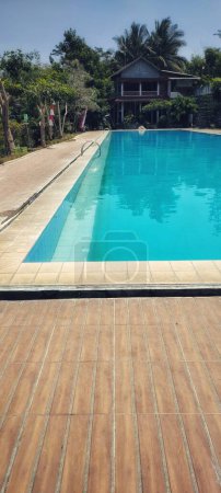 Téléchargez les photos : Portrait de piscine rectangulaire avec des bords en béton brun à une attraction touristique dans la campagne. Vacances avec vue imprenable, piscines et ciel bleu clair. - en image libre de droit