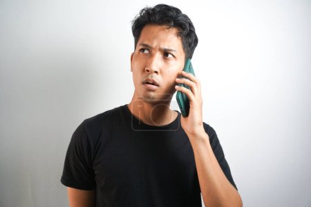 Photo for Young Asian Man is confused and shocked when calling in the phone. Indonesian man wearing a black shirt. - Royalty Free Image