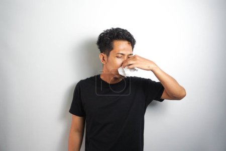 Photo for Young man has allergies coughs and sneezes is allergic to dust irritates his nasopharynx uses tissues to cover his snot : Asian man in poor health suffers from a respiratory disease. - Royalty Free Image