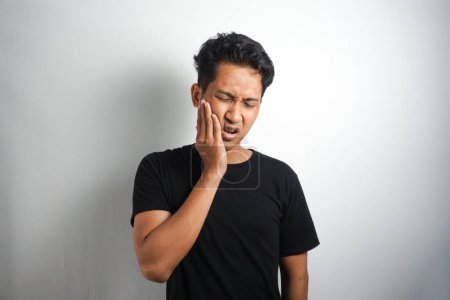 Photo for Portrait young man touch cheek. He has strong toothache and suffering from pain wearing casual white t-shirt against grey background. Feel toothache - Royalty Free Image