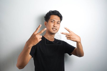 Photo for Photo of cheerful nice kind friendly asian man showing v-sign looking for friends in new town he has never been to before while isolated with white background - Royalty Free Image