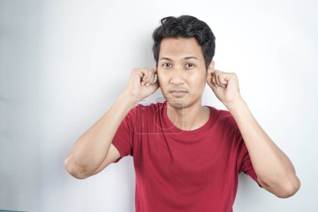 Photo for Young asian man wearing casual red t shirt covering ears with fingers with annoyed expression for the noise of loud music. deaf concept. - Royalty Free Image
