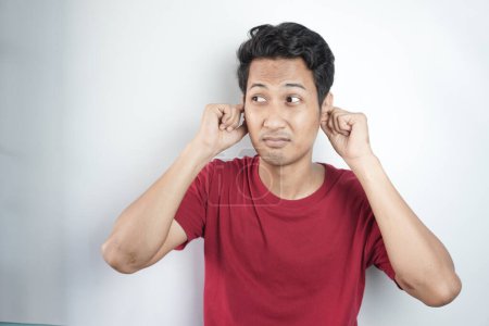 Photo for Young asian man wearing casual red t shirt covering ears with fingers with annoyed expression for the noise of loud music. deaf concept. - Royalty Free Image