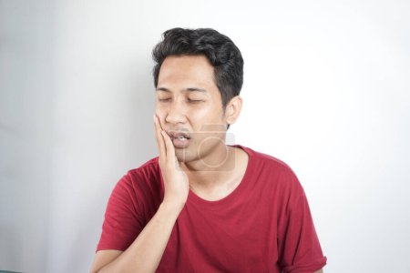 Photo for Tooth ache concept. Indoor shot of young male feeling pain, holding his cheek with hand, suffering from bad toothache, looking at camera with painful expression - Royalty Free Image